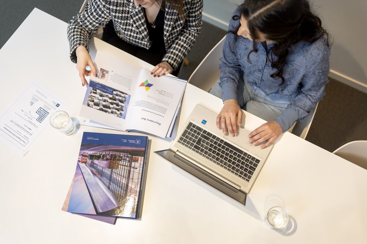 Vista superior da mesa com papéis, laptop e fichários.