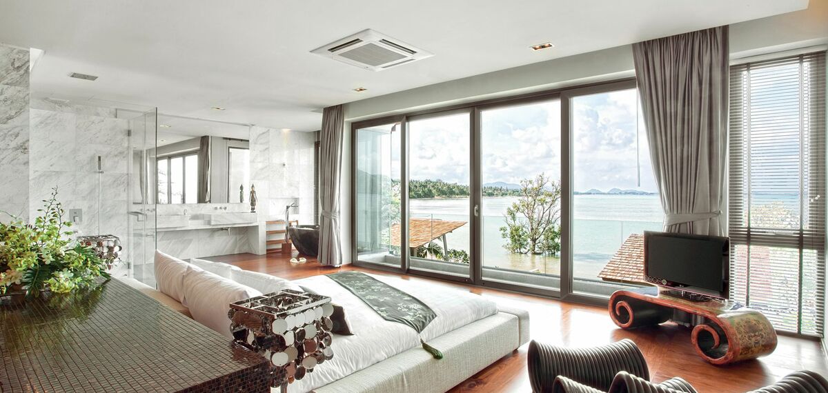 Interior view of a bedroom in the Eva Beach Resort in Thailand, with a Reynaers Aluminium lift-and-slide solution opening up to the beach and ocean.