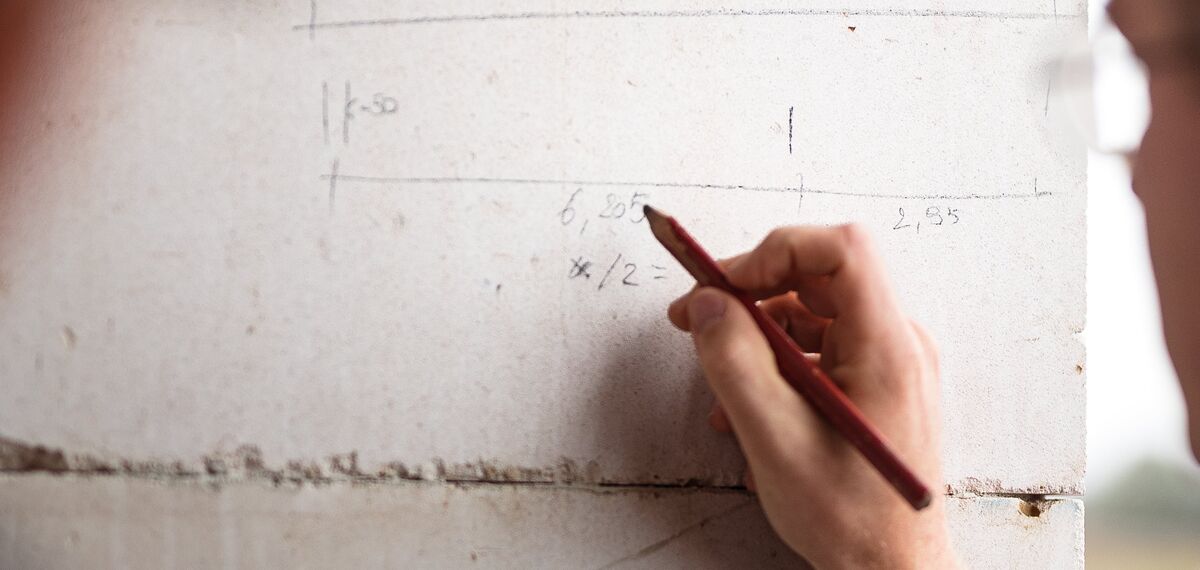 Homem escrevendo com lápis na parede de concreto do canteiro de obras.