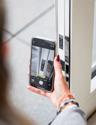 Mão a segurar um smartphone perto de um código QR numa janela branca Perfis.